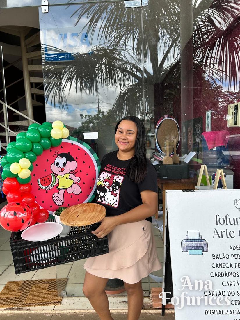 Ana segurando o kit pegue e monte do tema Magali, com painel e arco de balões